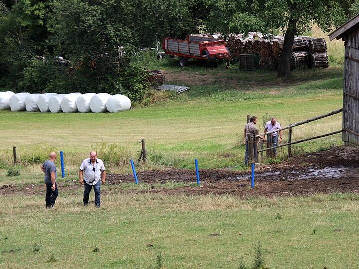 Polizisten in Zivil stehen auf einer Weide, auf der zuvor ein Stier zwei Menschen getötet hatte.