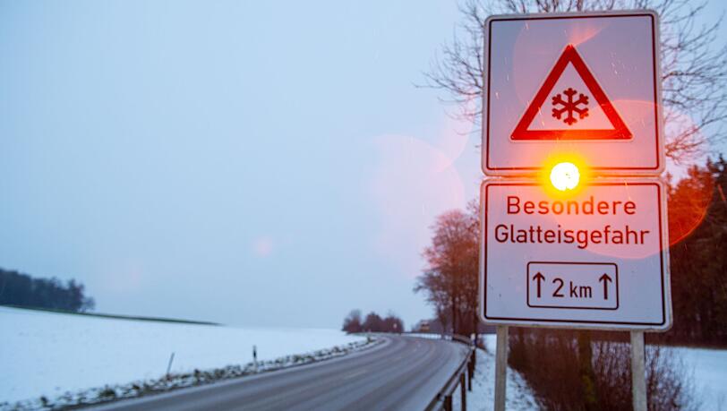 Ein Straßenschild warnt mit einer Blinkleuchte vor Glatteis.