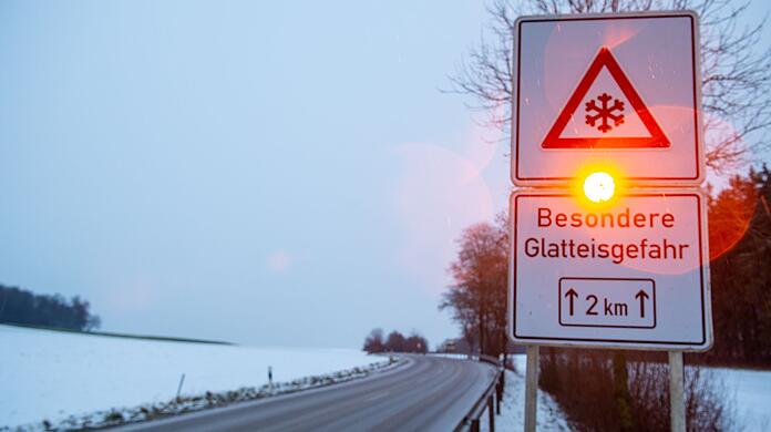 Ein Straßenschild warnt mit einer Blinkleuchte vor Glatteis.