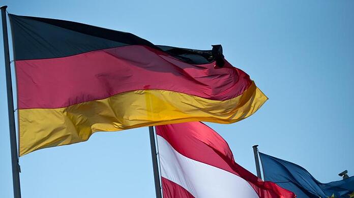 Die deutsche, die österreichische und die EU-Flagge wehen in Berlin vor dem Bundeskanzleramt.