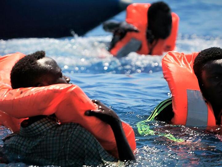 Flüchtlinge schwimmen mit Rettungswesten im Meer, bevor sie vom Rettungsschiff "Ocean Viking" aufgenommen werden.