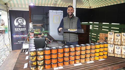 Baris Çelik verkauft auf dem Viktualienmarkt türkische Köstlichkeiten. Viele sind hausgemacht, von seiner Mutter. Sein Vater stand für das Standl-Logo (links) Modell.