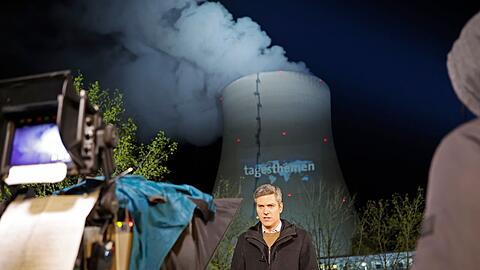 Moderator Ingo Zamperoni steht auf einem Balkon vor dem Kühlturm des AKW.