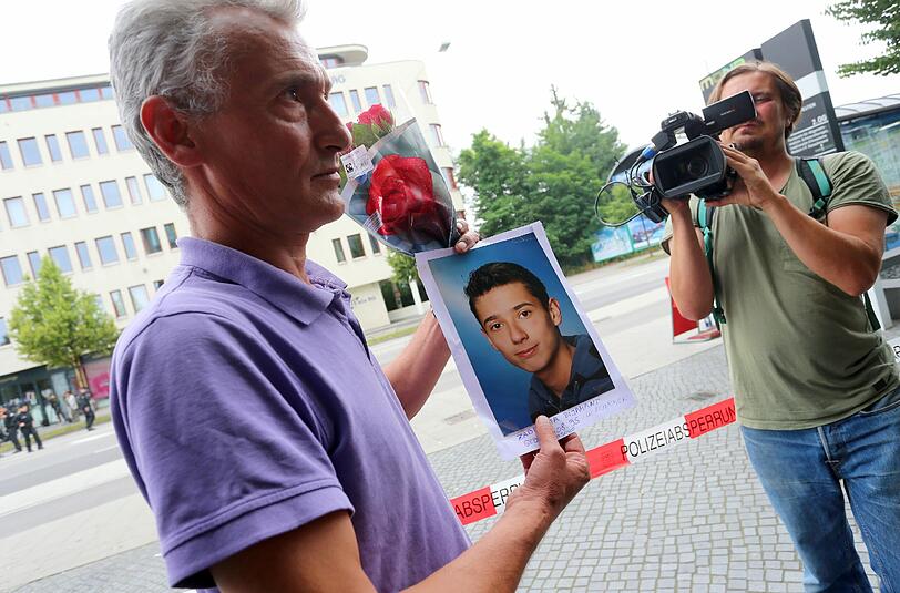 Naim Zabergja steht mit einem Foto seines getöteten Sohnes Dijamant am Olympia-Einkaufszentrum.
