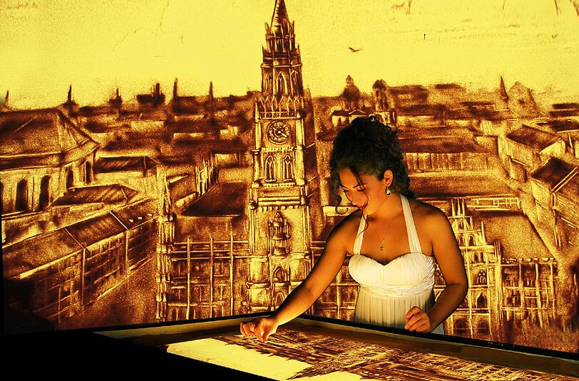 Die Künstlerin malt, eine Kamera filmt: So entstehen auf der Leinwand immer neue Sandbilder von München.