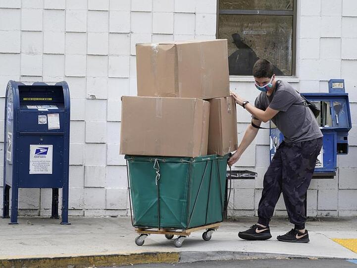 Ein Mann trägt eine Schutzmaske während er große Paketboxen von einem Postamt in Los Angeles in ein Fahrzeug transportiert.