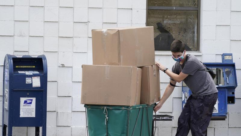 Ein Mann trägt eine Schutzmaske während er große Paketboxen von einem Postamt in Los Angeles in ein Fahrzeug transportiert. Ein Mann trägt eine Schutzmaske während er große Paketboxen von einem Postamt in Los Angeles in ein Fahrzeug transportiert.