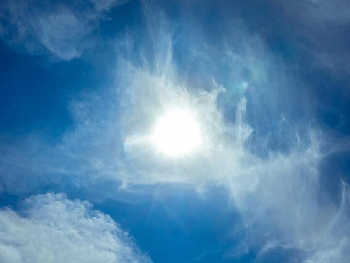 Die Sonne scheint am blauen Himmel durch Wolken hindurch. Foto: Markus Scholz/dpa/Symbolbild
