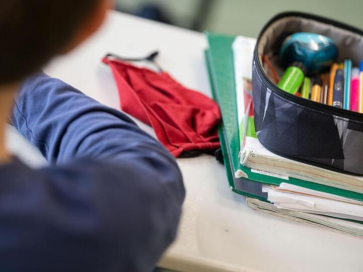 Die Mund-Nasen-Bedeckung eines Schülers liegt während des Unterrichts auf dem Tisch. Foto: Marijan Murat/dpa/Archiv/Symbolbild