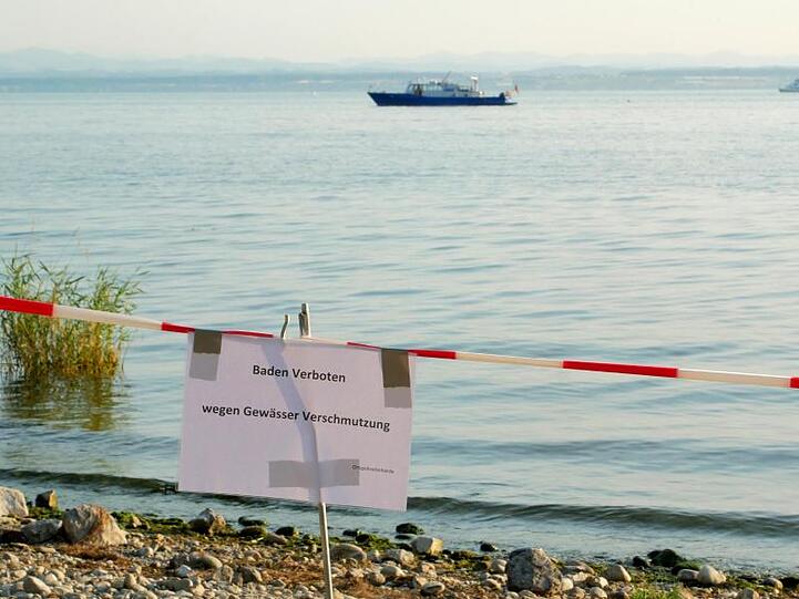 Ein Uferabschnitt am Bodensee bei Friedrichshafen ist mit einem Hinweisschild und einem Absperrband für Badegäste gesperrt. Foto: Marcus Fey