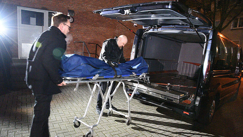 Zwei Männer bringen am Donnerstag die Leiche eines Mannes vom Tatort in einem Mehrfamilienhaus in Essen in den Leichenwagen.