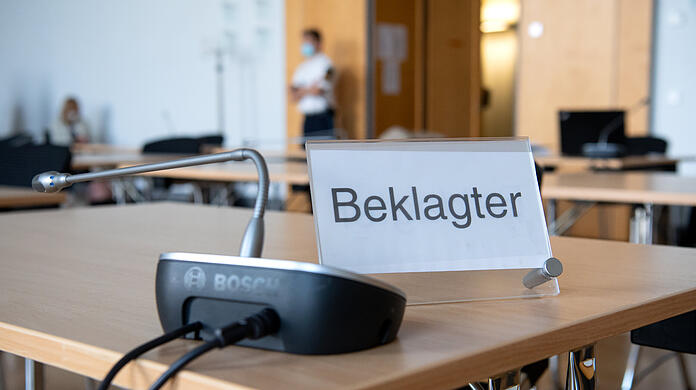 Ein Schild mit der Aufschrift "Beklagter" steht vor Verhandlungsbeginn in einem Gerichtssaal im Landgericht.