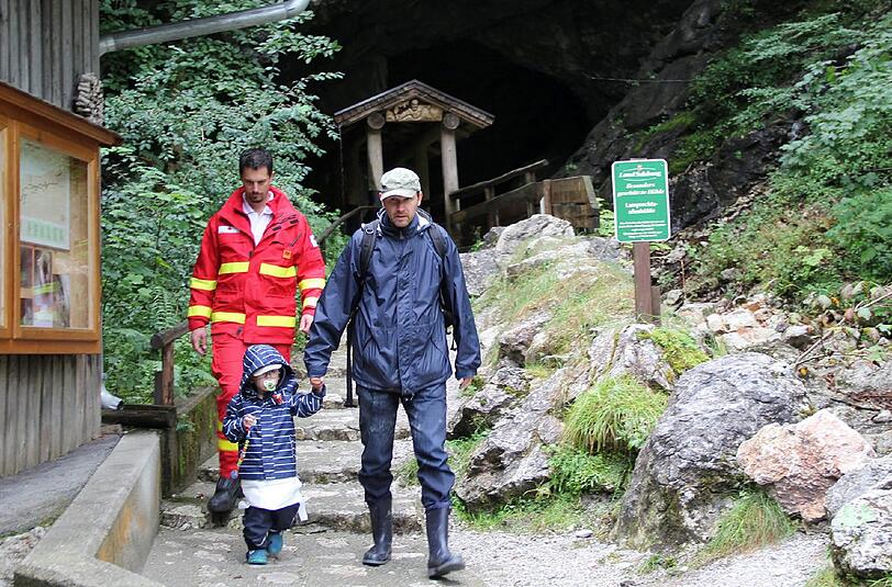 Ein Rettungssanitäter geleitet einen Mann und ein kleines Mädchen aus der Höhle.