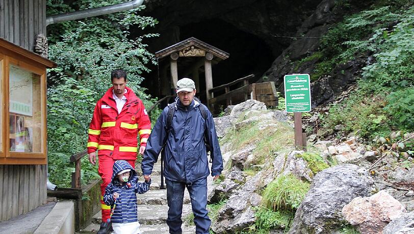 Ein Rettungssanitäter geleitet einen Mann und ein kleines Mädchen aus der Höhle. Ein Rettungssanitäter geleitet einen Mann und ein kleines Mädchen aus der Höhle.