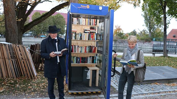 OB Alexander Putz und Peggy Füger, Präsidentin des Rotary Club Landshut/Trausnitz, machen eine Leseprobe bei der Einweihung der ersten Bücherzelle in Landshut.