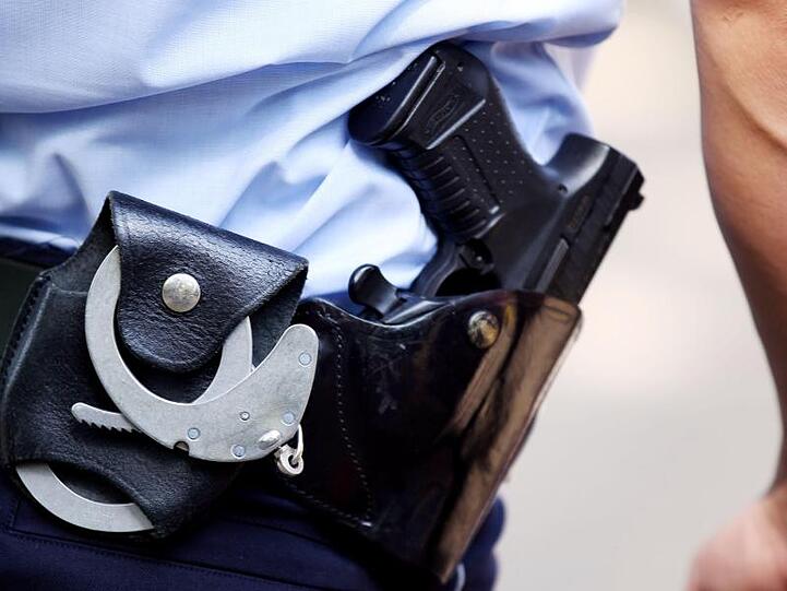 Ein Polizist mit Handschellen und Pistole am Gürtel. Foto: Oliver Berg/dpa/Archivbild