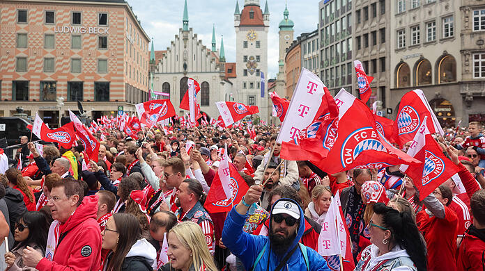 Die Fans des FC Bayern  schwenken Fahnen und warten auf den Beginn der Meisterfeier am Marienplatz.