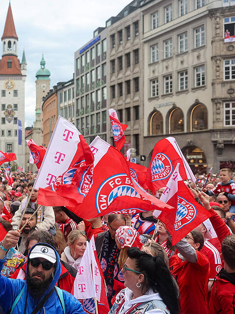 Die Fans des FC Bayern  schwenken Fahnen und warten auf den Beginn der Meisterfeier am Marienplatz.