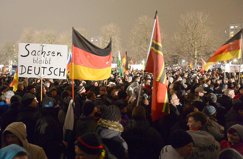 Teilnehmer der islamkritischen Pegida-Bewegung halten am 05.01.2015 Deutschland-Fahnen und ein Plakat mit der Aufschrift «Sachsen bleibt DEUTSCH» bei einer Kundgebung in Dresden (Sachsen). Die Pegida hat zu einer erneuten Demonstration in Sachsens Landeshauptstadt aufgerufen.