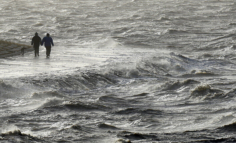 Passanten trotzen am Nordseedeich dem Sturm. Gleich zwei Orkanausläufer werden am Wochenende den Norden streifen.