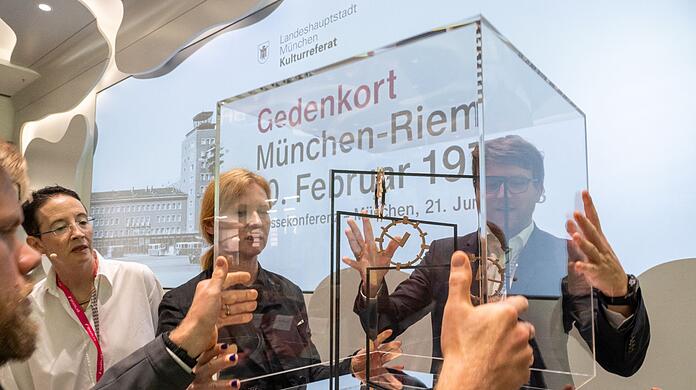 Die Künstlerin Alicja Kwade (M.) nimmt die Glaskuppel vom Modell für den Gedenkort "Riem 1970" ab.
