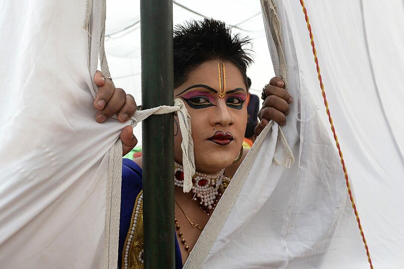 Ein als Gottheit verkleideter Hindu blickt aus einem Zelt in Neu Delhi vor einer Prozession zu Ehren des Hindu-Gottes Hanuman.