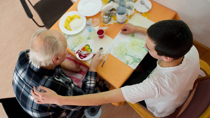 Ein Helfer hilft einem Senioren beim Essen. Vielerorts fehlen jedoch Pflegekräfte, auch die Qualität der Ausbildung wird schlechter.