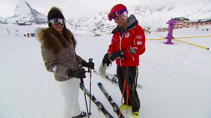 Joanna steht mit wackeligen Knien auf ihren Brettern. Sie bekommt extra einen Privatlehrer, der ihr das Skifahren beibringen soll.