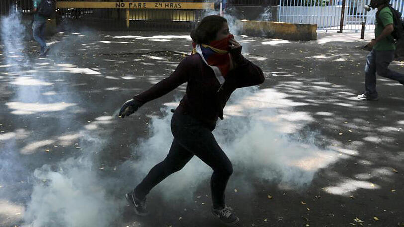 Ein Demonstrant schmeißt einen Tränengaskanister auf Polizisten während der Proteste in Caracas.