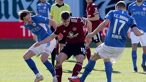 Nürnbergs Fabian Nürnberger wird im Kampf um den Ball von Rostocks Bentley Baxter Bahn (l) und Hanno Behrens gedoppelt.