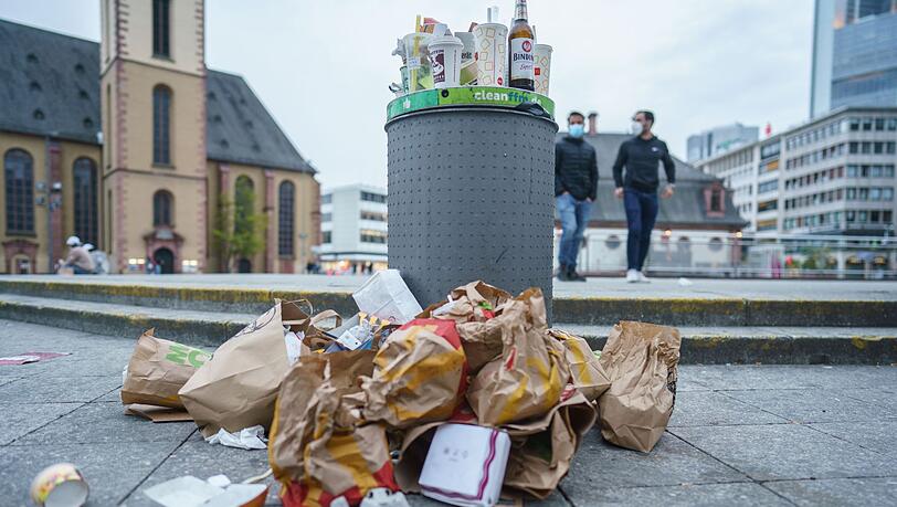 Müll liegt in der Innenstadt neben einem überfüllten Abfallbehälter.