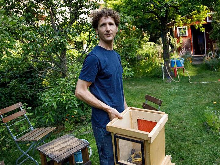 Der Imker Jonas Hörning hält einen Bienenkasten, um einen herrenlosen Bienenschwarm in einer Kleingartenanlage einzufangen.