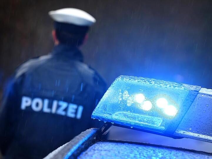 Ein Polizist steht im Regen vor einem Streifenwagen dessen Blaulicht aktiviert ist. Foto: Karl-Josef Hildenbrand/dpa/Archivbild