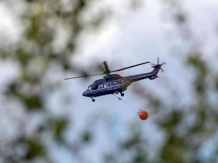 Ein Hubschrauber der Bundespolizei transportiert Löschwasser zu einem Brandherd.