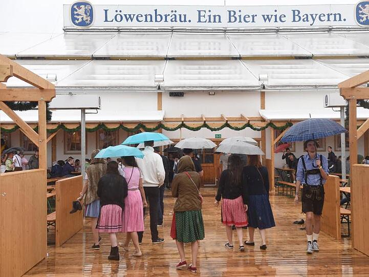 Gäste mit Regenschirmen gehen in München (Bayern) auf dem Oktoberfest in das Löwenbräuzelt. Foto: Felix Hörhager/Archiv