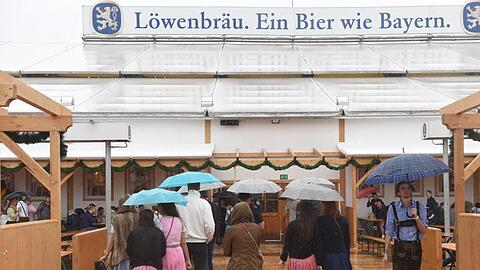 Gäste mit Regenschirmen gehen in München (Bayern) auf dem Oktoberfest in das Löwenbräuzelt. Foto: Felix Hörhager/Archiv