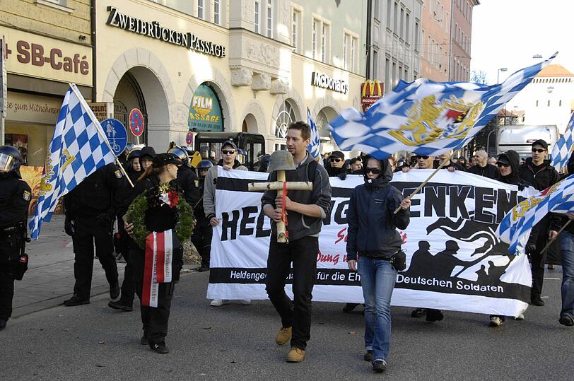 Gespenstisch: Neonazis tragen bei einem &bdquo;Heldengedenkmarsch&ldquo; Stahlhelme durch die Straße und schwenken die bayerische Flagge.