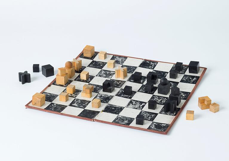 Auf diese Idee muss man erst einmal kommen: nämlich Schachfiguren nach der Art ihrer Spielzüge zu gestalten. 1924 stellte der Bildhauer Josef Hartwig seine auf abstrakte Formen reduzierten Spielsteine vor. Der Springer &ndash; normalerweise ein Pferd &ndash; bewegt sich rechtwinklig in Hakenform, also zeigt Hartwigs Version eine rechtwinklige Würfelanordnung. Und der Läufer, der diagonal zum Brett zieht, weist ein Schrägkreuz auf, das aus einem Würfel geschnitten ist. Hartwigs Schachspiel gehörte zu den erfolgreichsten Produkten des Bauhauses und wurde in drei Varianten hergestellt. Die Neue Sammlung besitzt die preisgünstigste mit einem Brett aus Pappkarton.