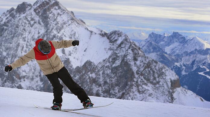 Ein Snowboarder fährt auf der Zugspitze vor dem Panorama der Alpen.