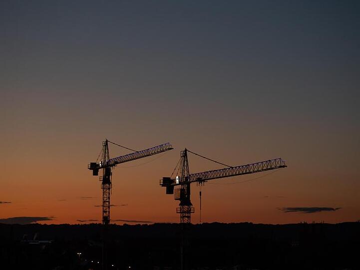 Kräne stehen vor dem Abendhimmel auf einer Baustelle. Foto: Robert Michael/dpa-Zentralbild/dpa/Symbolbild