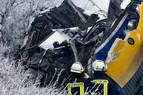 Einsatzkräfte stehen am Wrack einer Lokomotive