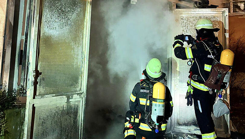 Feuerwehr l&ouml;schen mit Atemschutzmasken den Brand in dem M&uuml;llsammelh&auml;uschen.