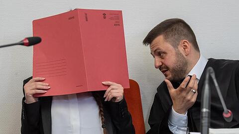 Die Angeklagte hält einen roten Aktendeckel vor ihr Gesicht.