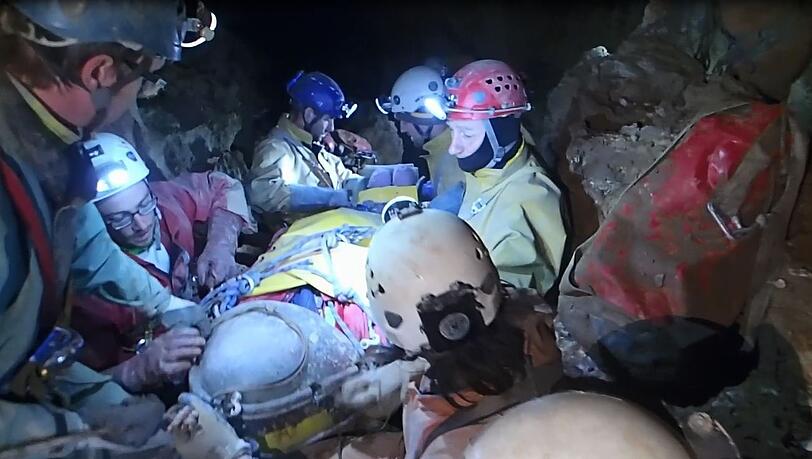 Zig Helfer umgeben den Verletzten im Höhlen-Inneren. Zig Helfer umgeben den Verletzten im Höhlen-Inneren.