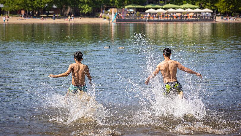 Zwei junge Männer rennen bei sonnigem Wetter in das Wasser eines Sees.