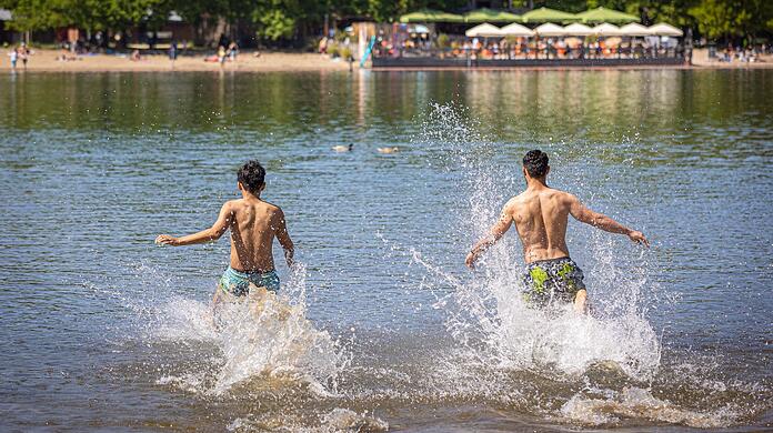 Zwei junge Männer rennen bei sonnigem Wetter in das Wasser eines Sees.