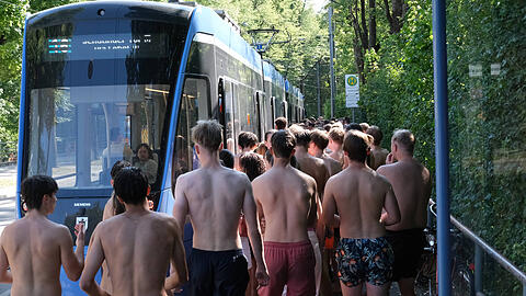 M&uuml;nchner fahren nach dem Abk&uuml;hlen im Eisbach in Badekleidung mit der Tram &ndash; eine sommerliche Tradition in der Stadt.