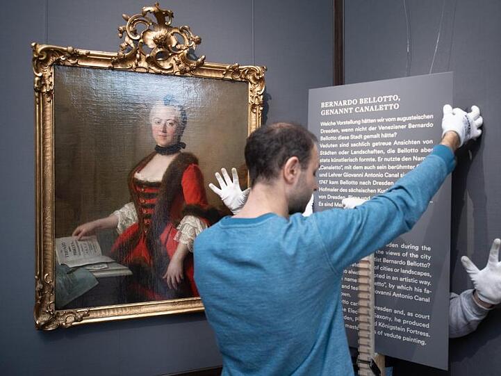 Mitarbeiter der Staatlichen Kunstsammlungen hängen eine Texttafel neben dem Ölgemälde "Maria Antonia von Bayern" von Pietro Antonio Graf Rotarie auf.