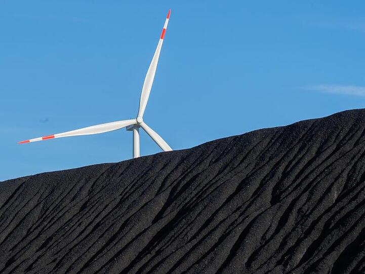 Steinkohle lagert im Hafen des Kraftwerks Mehrum in Niedersachsen - dahinter erhebt sich ein Windrad.