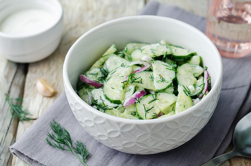 Eine cremige Alternative ist der Gurkensalat mit Joghurt und Dill im Tzatziki-Style. Daf&uuml;r schneiden Sie zuerst zwei gro&szlig;e Salatgurken in feine Scheiben. Anschlie&szlig;end mischen Sie einen halben Teel&ouml;ffel Salz unter die Gurken und lassen alles etwa 15 Minuten ziehen, damit &uuml;bersch&uuml;ssige Fl&uuml;ssigkeit austritt. Dann dr&uuml;cken Sie die Gurken gr&uuml;ndlich aus und gie&szlig;en das Wasser ab.
